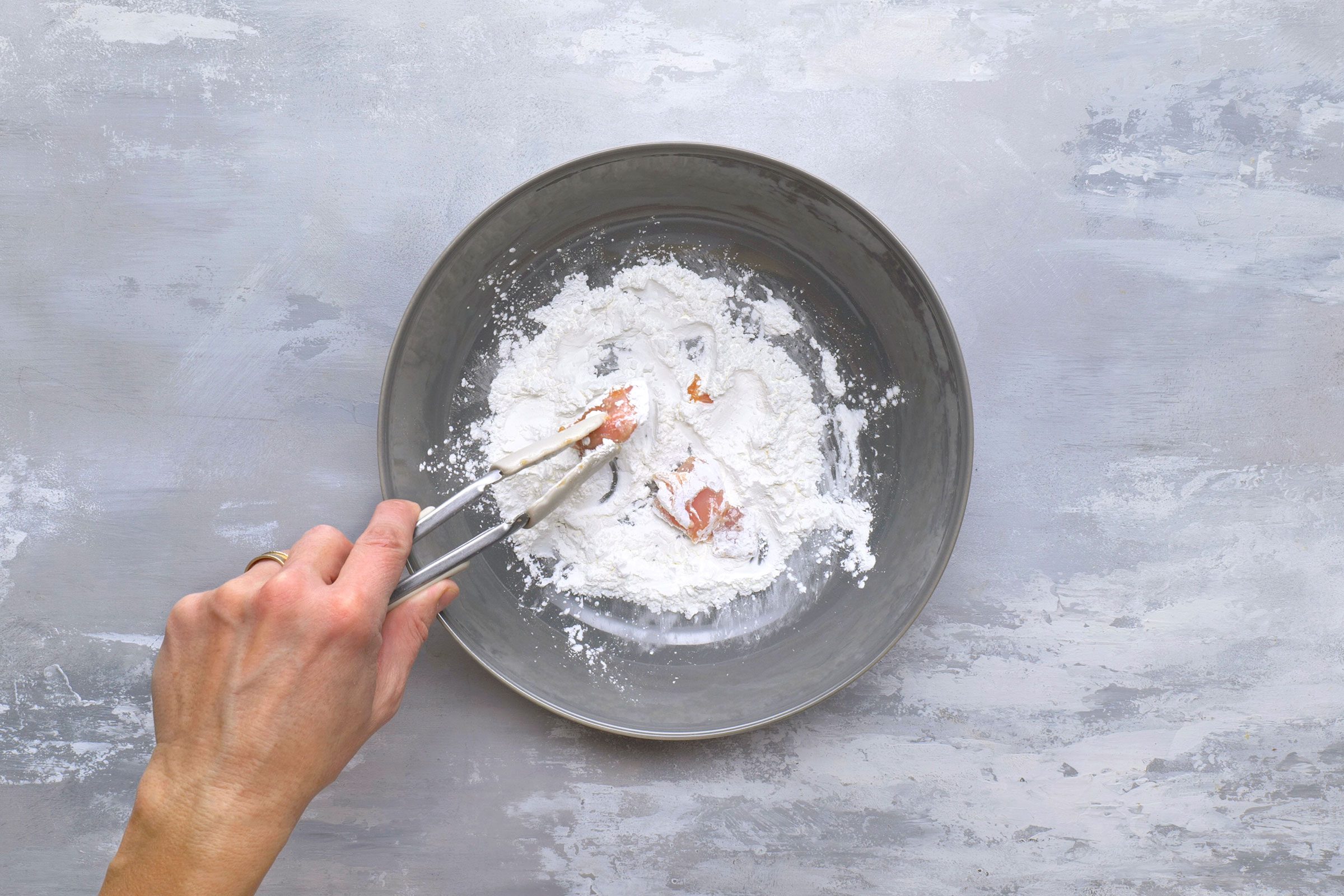 Tossing and coating marinated chicken pieces in cornstarch in a skillet