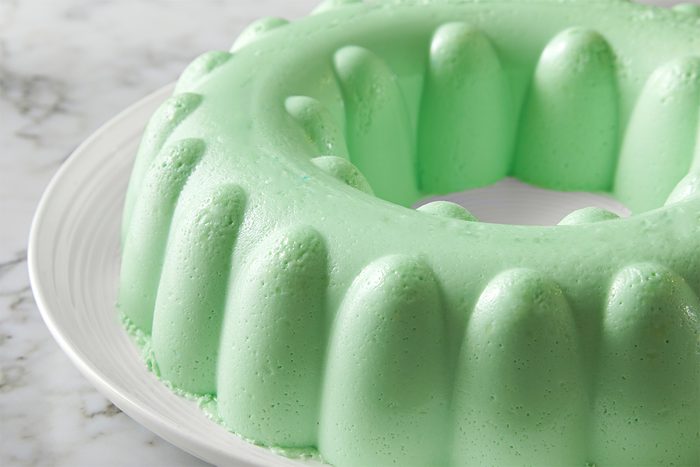 Side view of firm lime gelatin salad served on a white plate kept on top of a white marbletop.