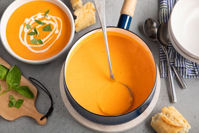 A steaming bowl of roasted red pepper soup with a spoon placed next to it, perfect for a cozy meal