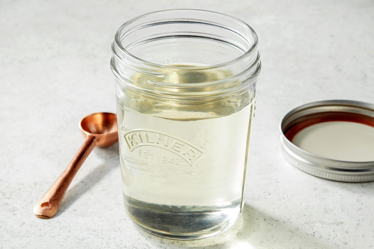Table view shot of Homemade Simple Syrup; in a container with a tight-fitting lid; spoon; marble surface