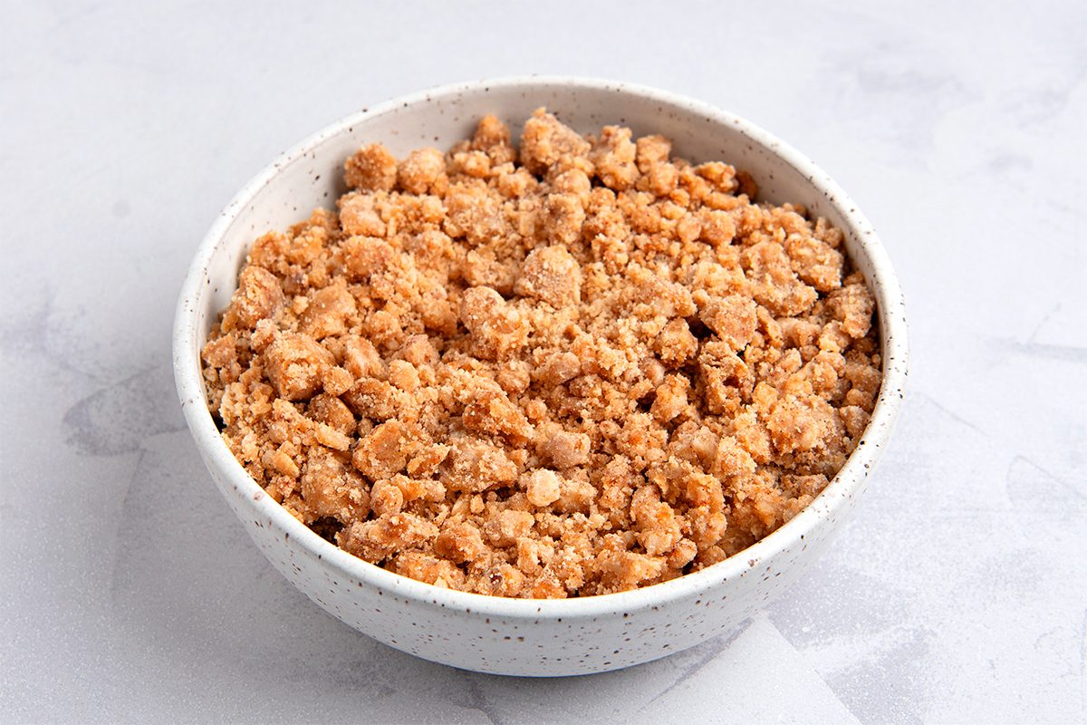 A white speckled bowl filled with crumbled, cooked ground meat or plant-based protein sits on a light gray surface. The texture is crumbly and golden brown.