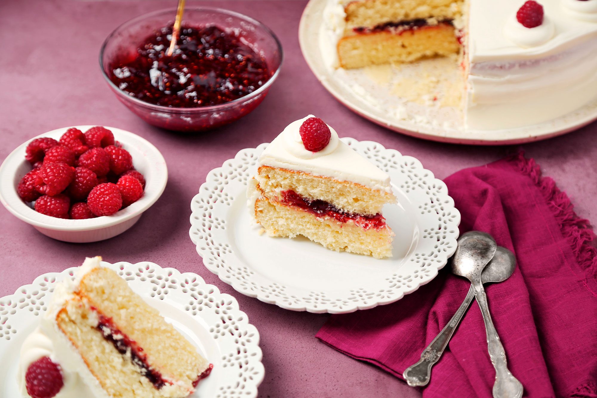 White chocolate Raspberry Cake shot on a magenta surface. Cake sliced and served on white lace placed