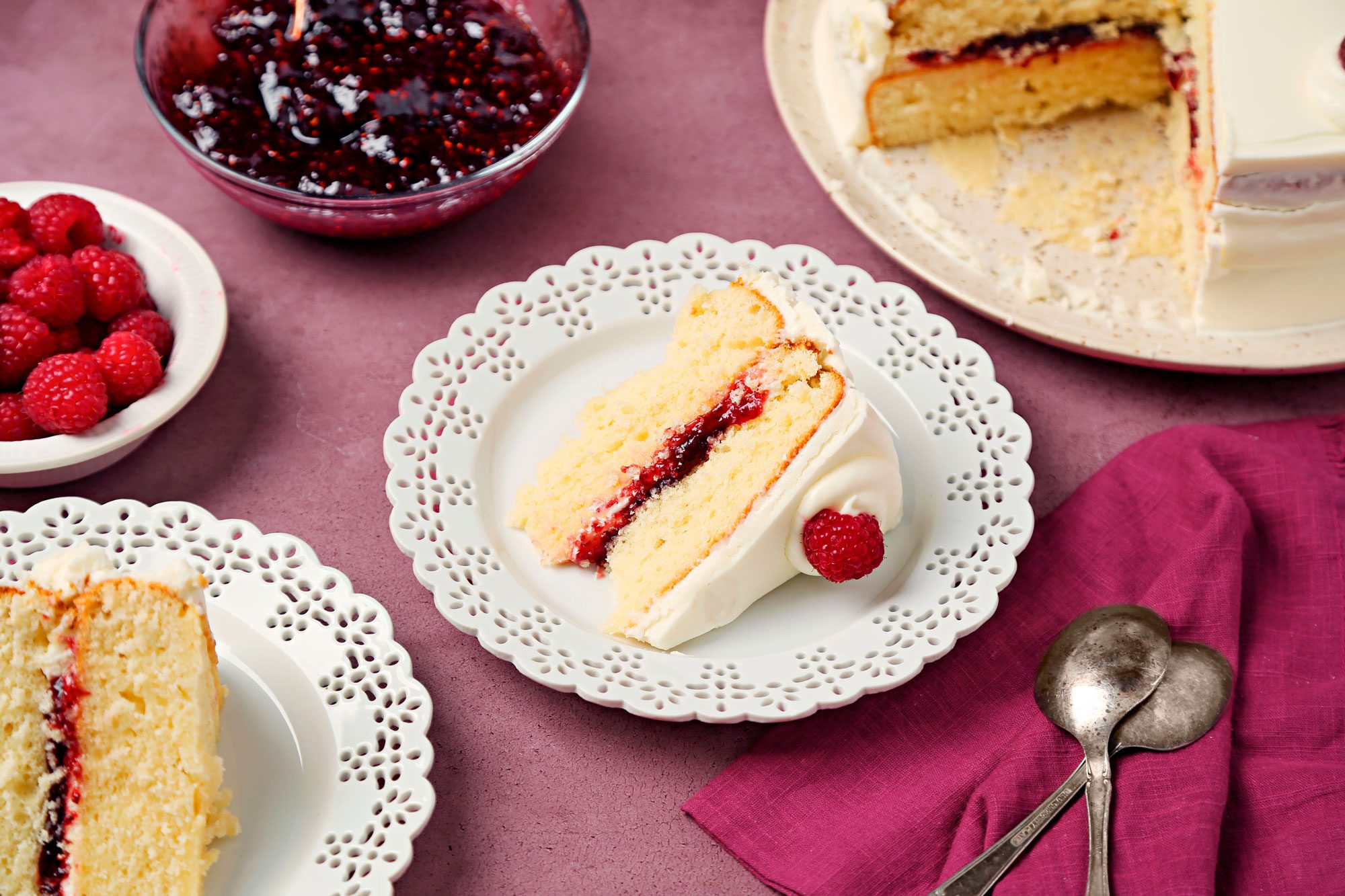 White chocolate Raspberry Cake shot on a magenta surface. Cake sliced and served on white lace placed