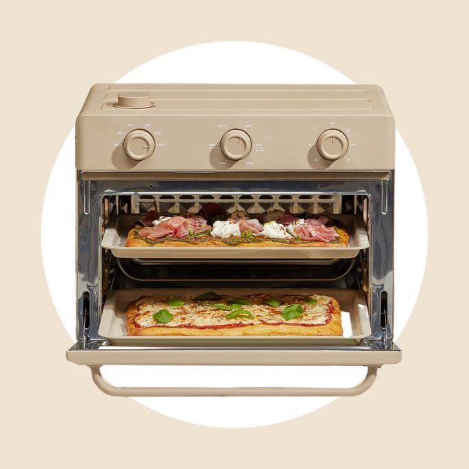 Open tan air fryer oven with two pizzas on a tan and white background