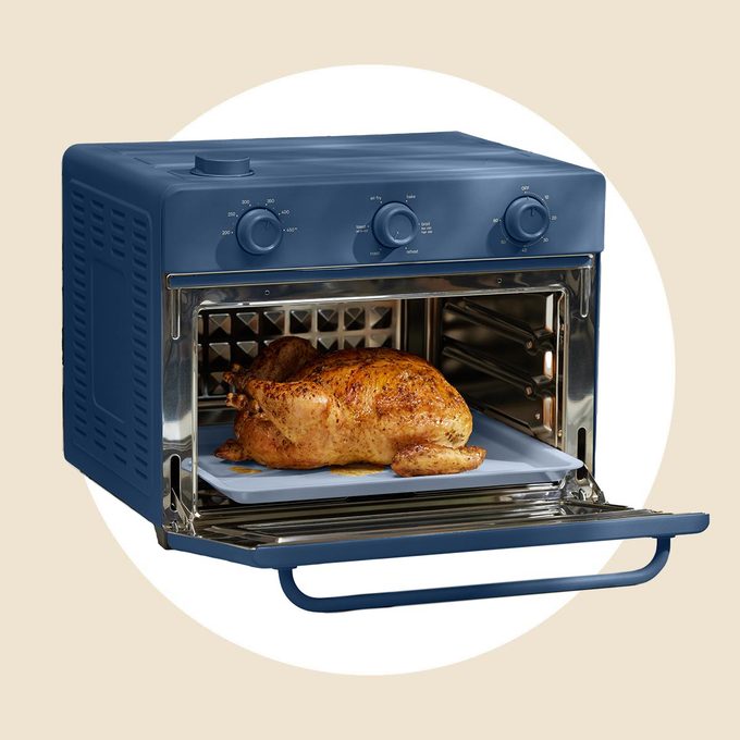 Open blue oven with a cooked chicken inside, on a white and tan background