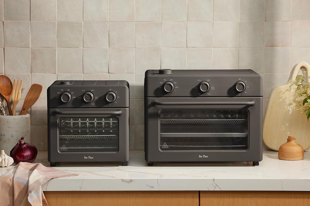 Small and large black ovens side-by-side on a kitchen counter, with a stone background and kitchen tools on either side