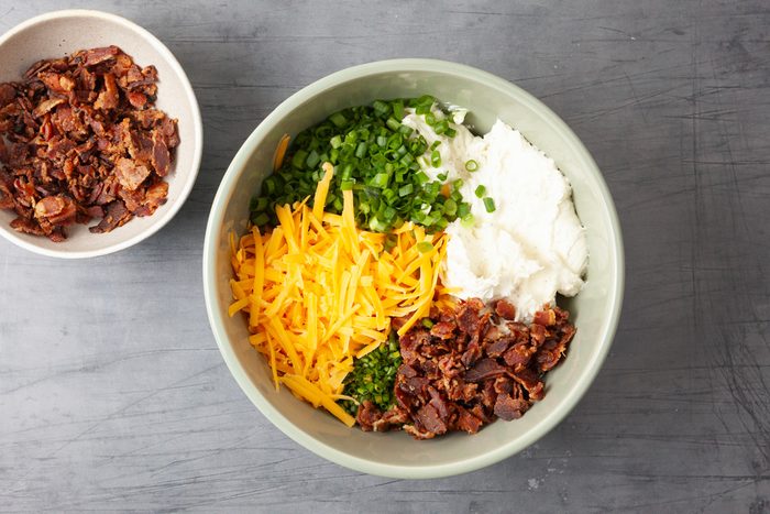 Overhead shot of a large bowl; beat cream cheese and ranch dip mix on medium speed until smooth 3-4 minutes; stir in shredded cheese; 1/3 of the crumbled bacon; green onion and chives until well combined; grey surface