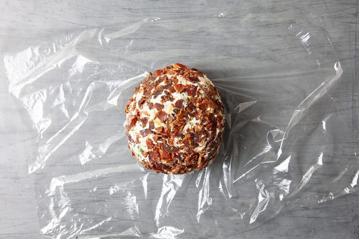 Overhead shot of roll into a ball; roll into remaining crumbled bacon so it covers the outside of the cheese ball; Wrap in plastic wrap; refrigerate at least 1 hour; grey surface