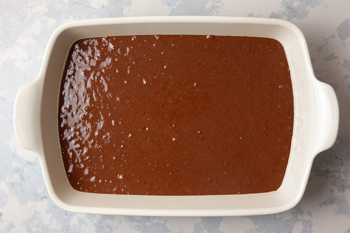 A white rectangular baking dish filled with smooth, glossy chocolate cake batter, resting on a light gray marbled surface.