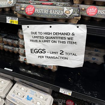 Sign indicating a limit of two egg cartons per shopper at a grocery store, in front of the egg shelves