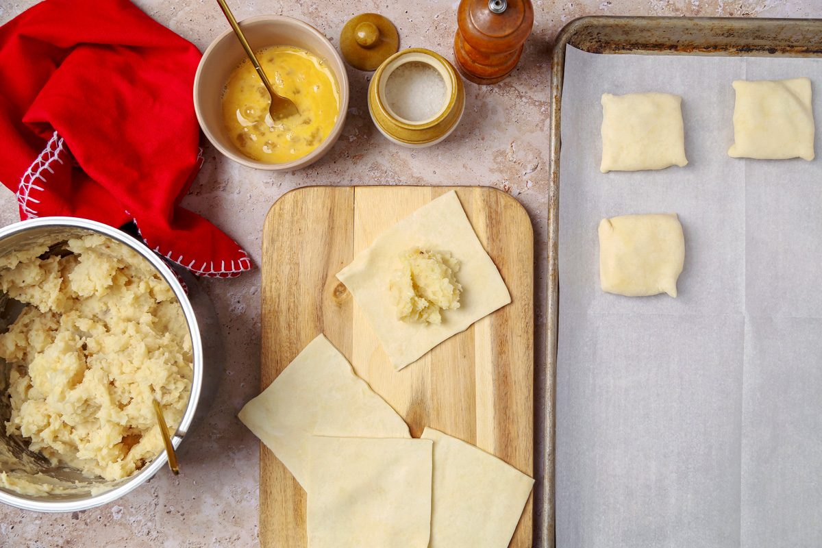 potato filling being spooned onto square shaped dough on a chopping board
