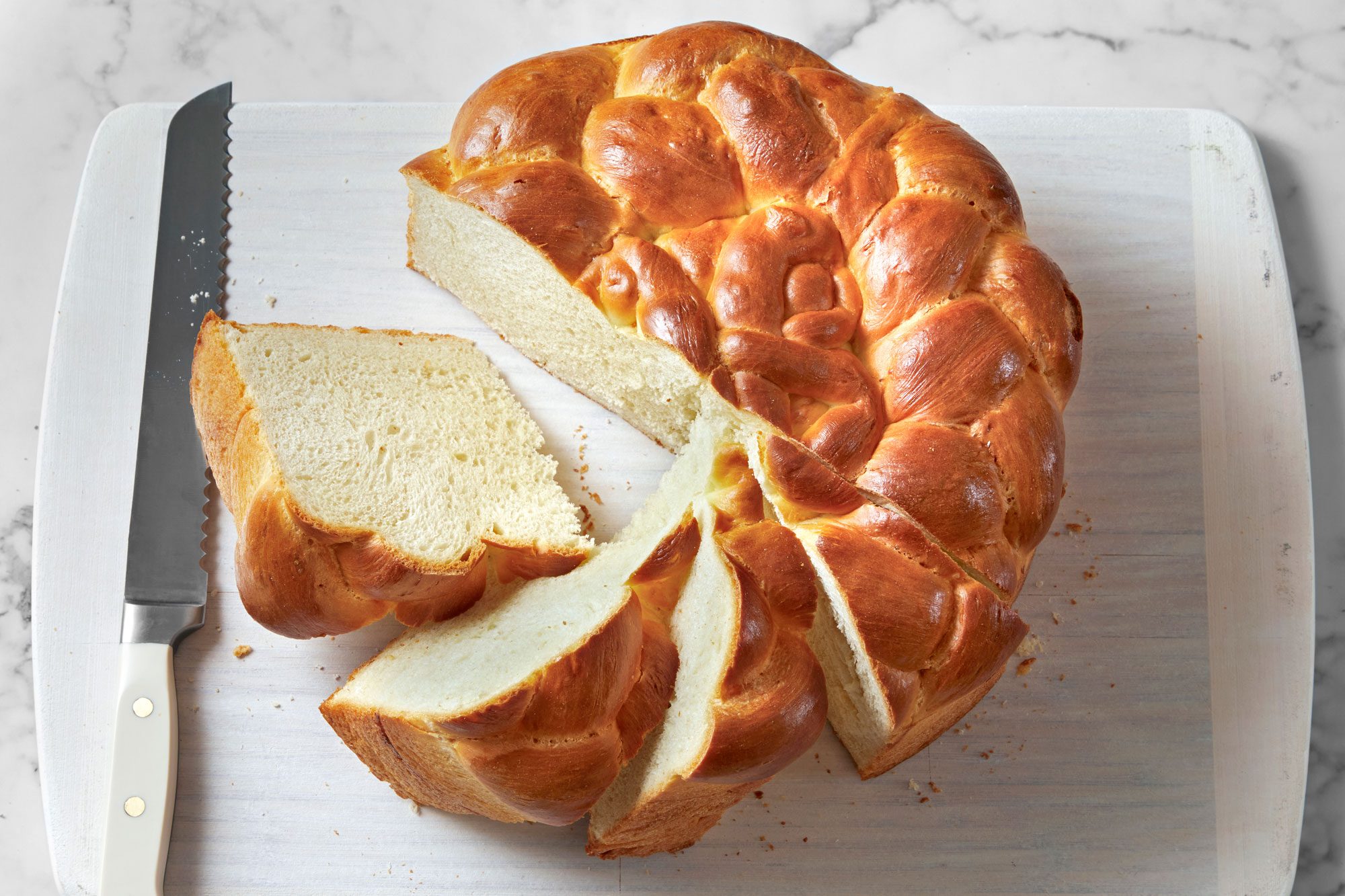 Overhead shot of Paska Easter Bread; serve on wooden tray; cut into slices; knife; marble surface