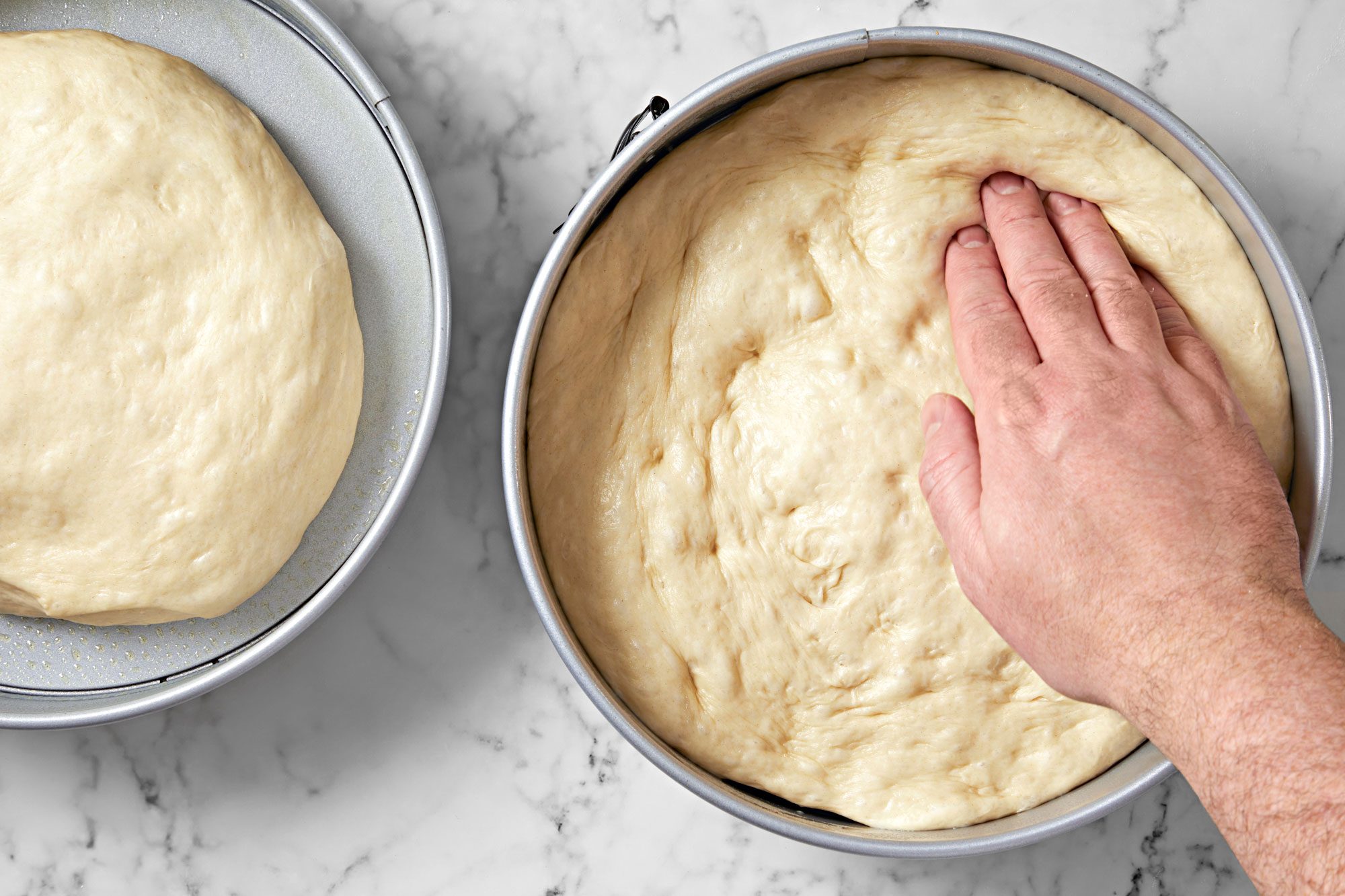 Overhead shot of punch dough down; Turn out onto a lightly floured surface; divide in half and set 1 portion aside; Divide remaining portion in half; press each portion into a well-greased 10-inch springform pan; marble surafce