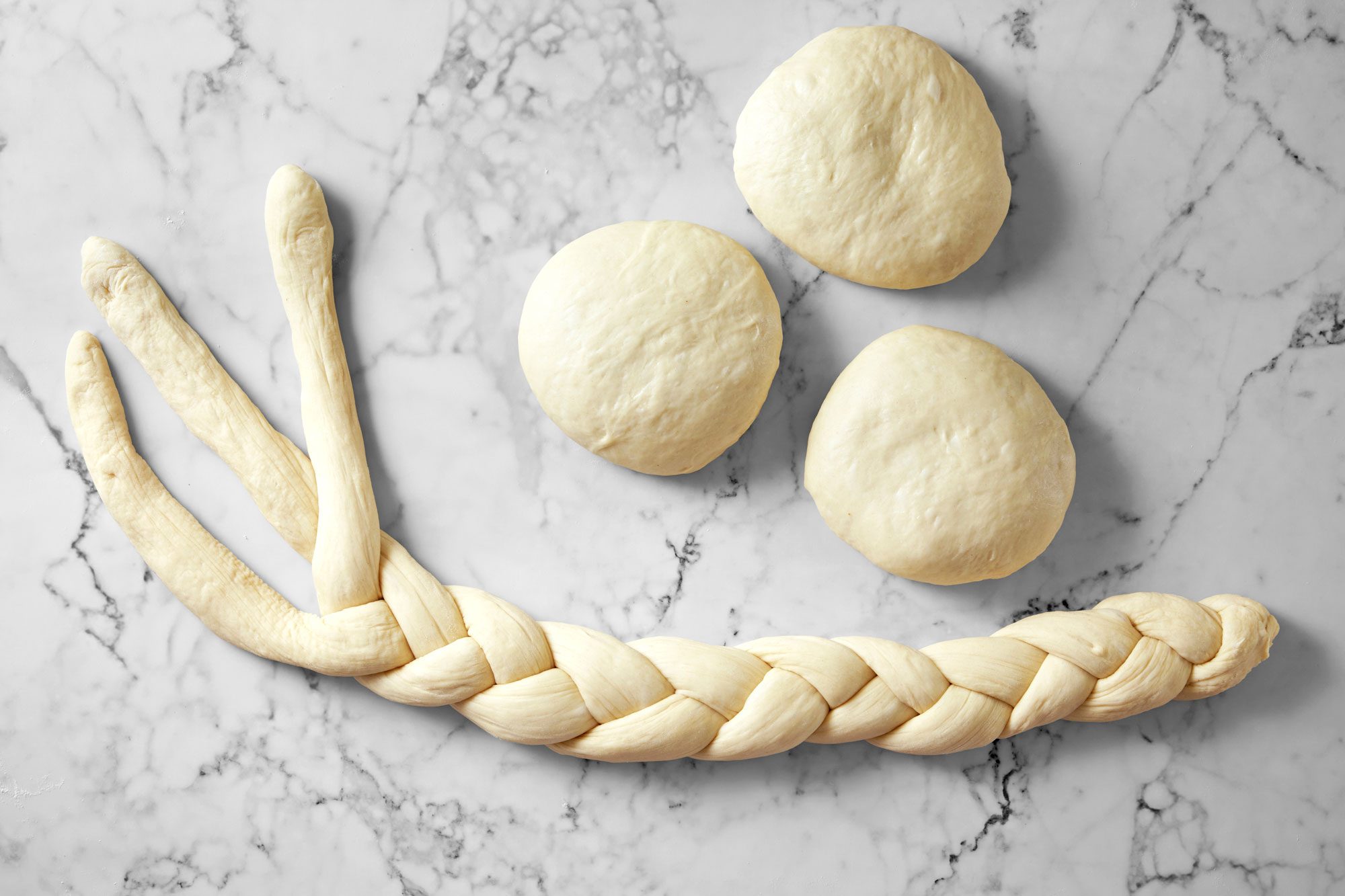 Overhead shot of divide reserved dough into 6 balls; Shape each ball into a 30-inch rope; make 2 braids of 3 ropes each; marble surface