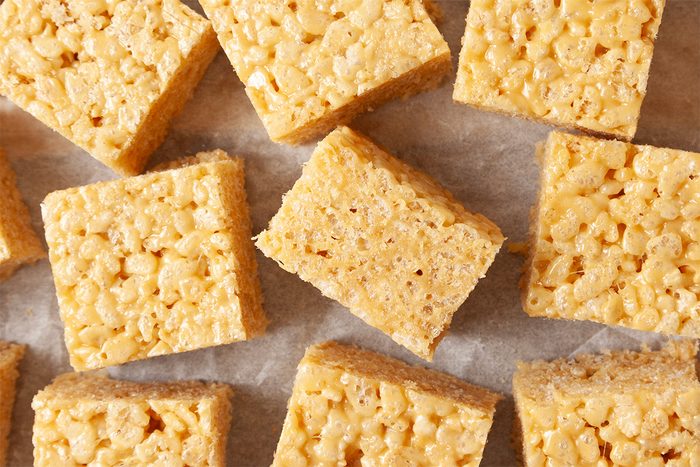 Close-up of several square rice crispy treats on wax paper. The treats have a golden, crispy texture and are aligned neatly.