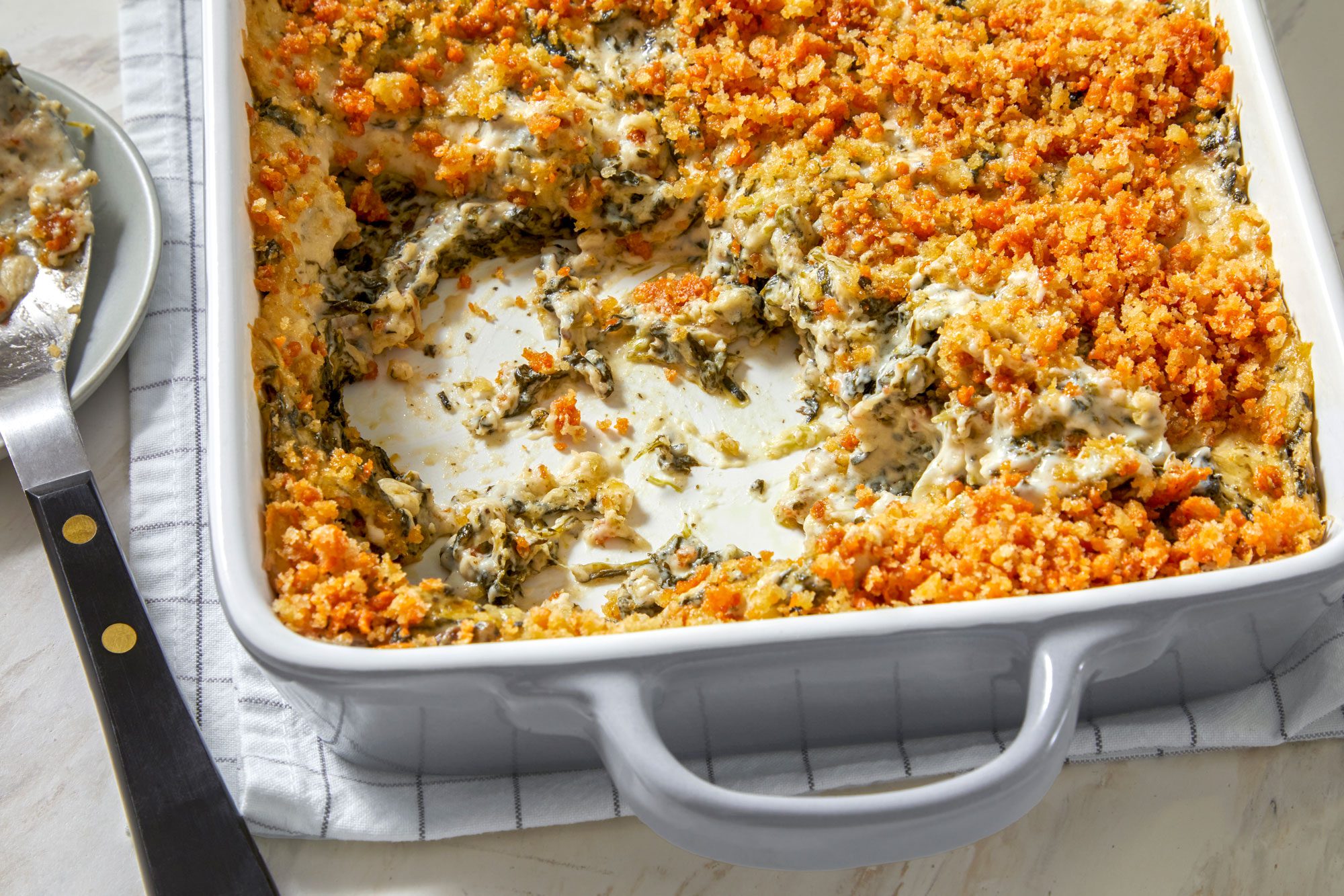Close shot of Easy Spinach Casserole in a baking pan with spoon and napkin on a marble surface