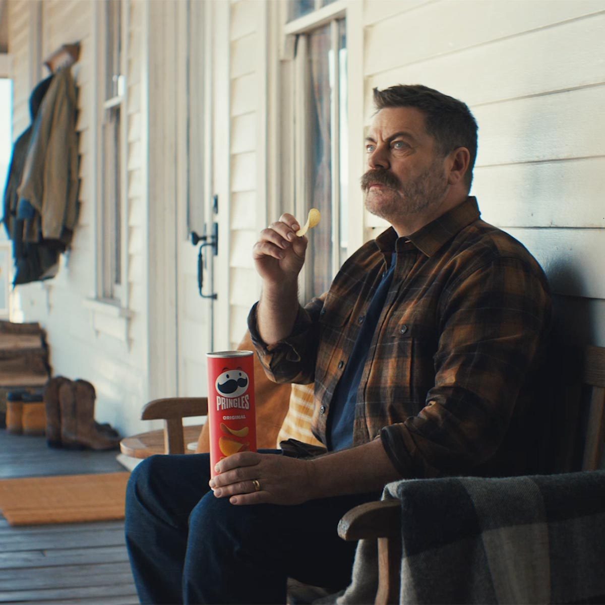 Nick Offerman sits on a porch eating pringles