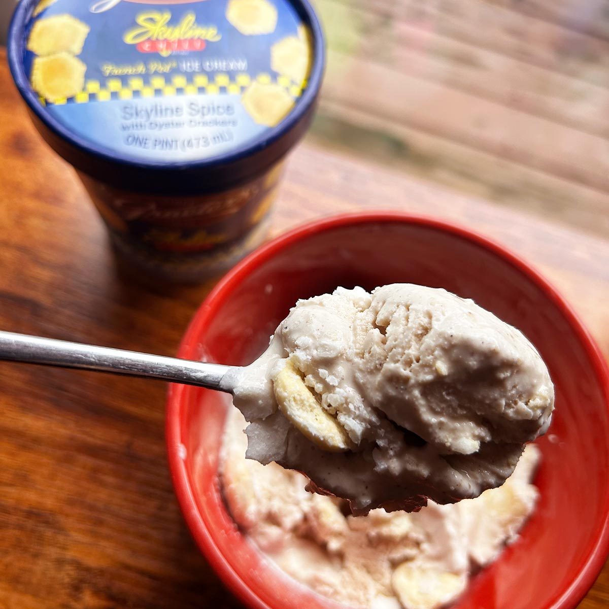 Birds eye view of a pint of Skyline Chili Ice Cream on the top left, with the ice cream in a red bowl to the bottom right and a close-up angle of a spoon of ice cream above it